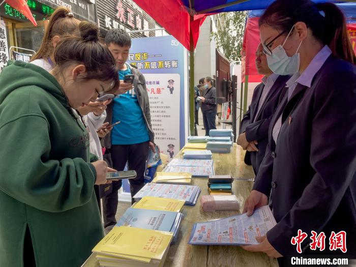 图为工作人员正在向路过市民介绍国家反诈中心软件的功能。　谢牧 摄
